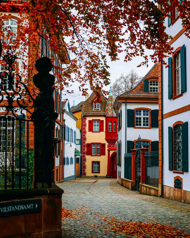 A cobbled lane in Basel Old Town with colourful historic houses and autumn leaves.