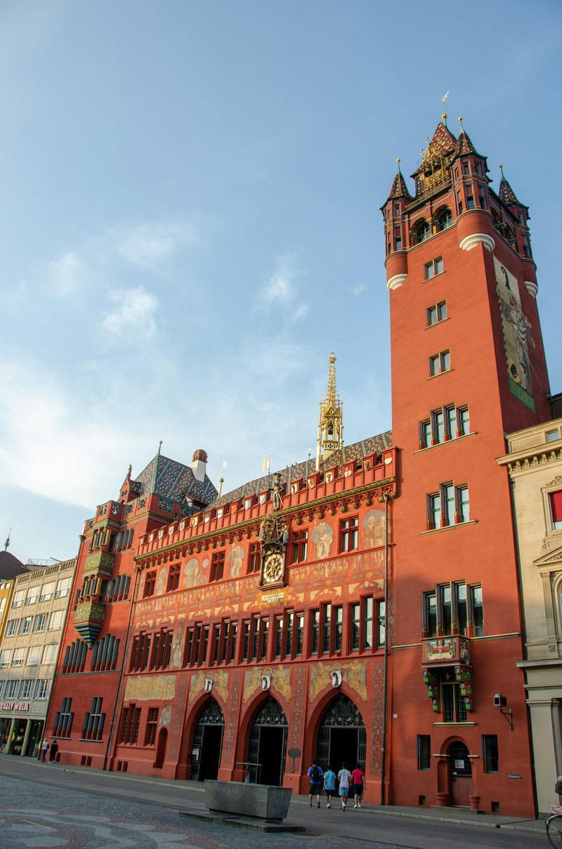 The red tower and painted façade of Basel Rathaus against a blue sky.