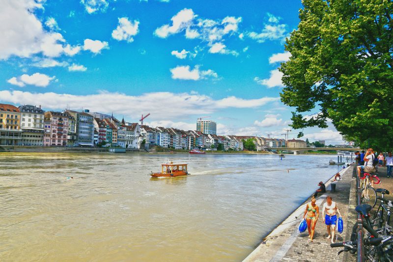 The Rhine in Basel on a sunny day, with a small boat and the riverside promenade.