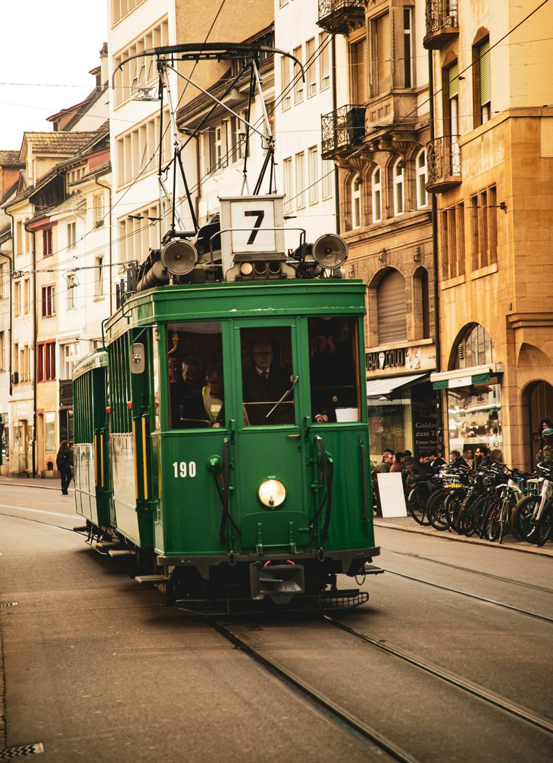 A vintage green Basel tram on line 7 in a street of historic buildings.
