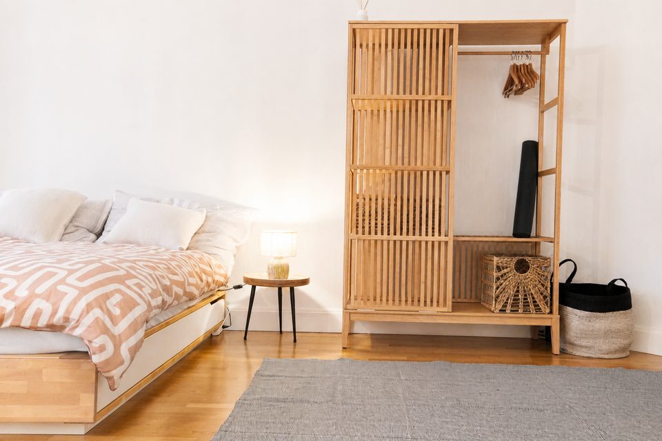 Double bed with terracotta patterned bedding, a small bedside lamp and an open slatted wooden wardrobe with hangers.