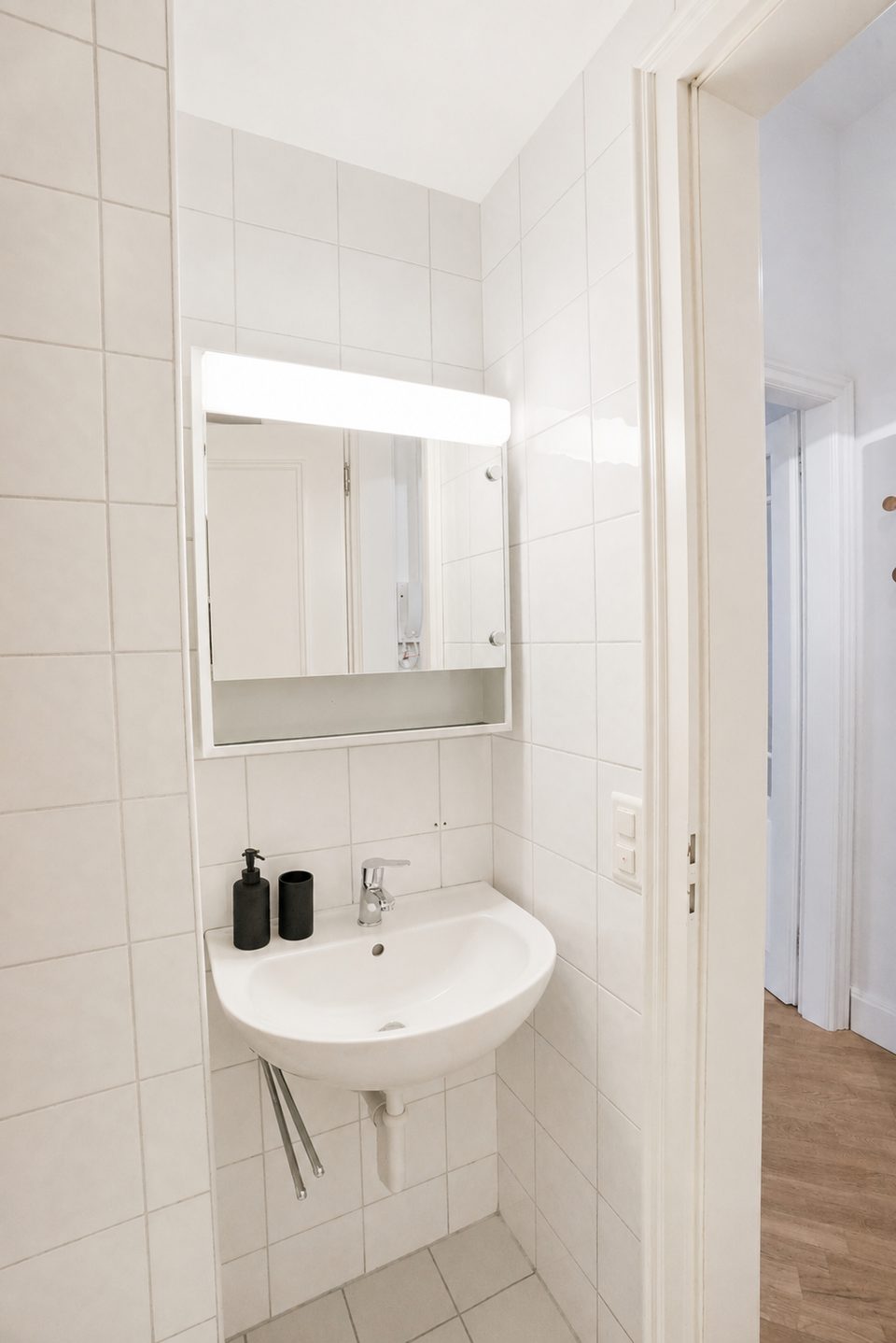 Wall-mounted washbasin beneath an illuminated mirror cabinet in the tiled bathroom.